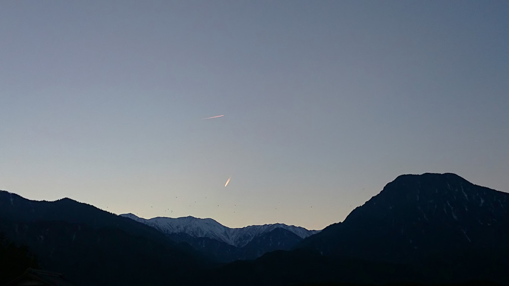 暮れ時の有明山と大天井岳の上を飛ぶ飛行機